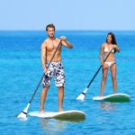Man and woman stand up paddleboarding on ocean. Young couple are doing watersport on sea. Male and female tourists are in swimwear during summer vacation.
