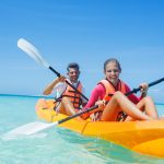 Happy cute girl and her father kayaking at tropical sea on yellow kayak