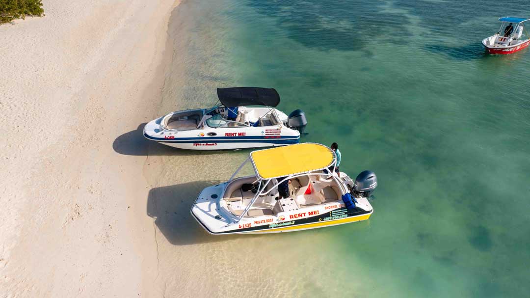 Two Come & Enjoy charter boats anchored in shallow turquoise water off a white sand beach in Aruba