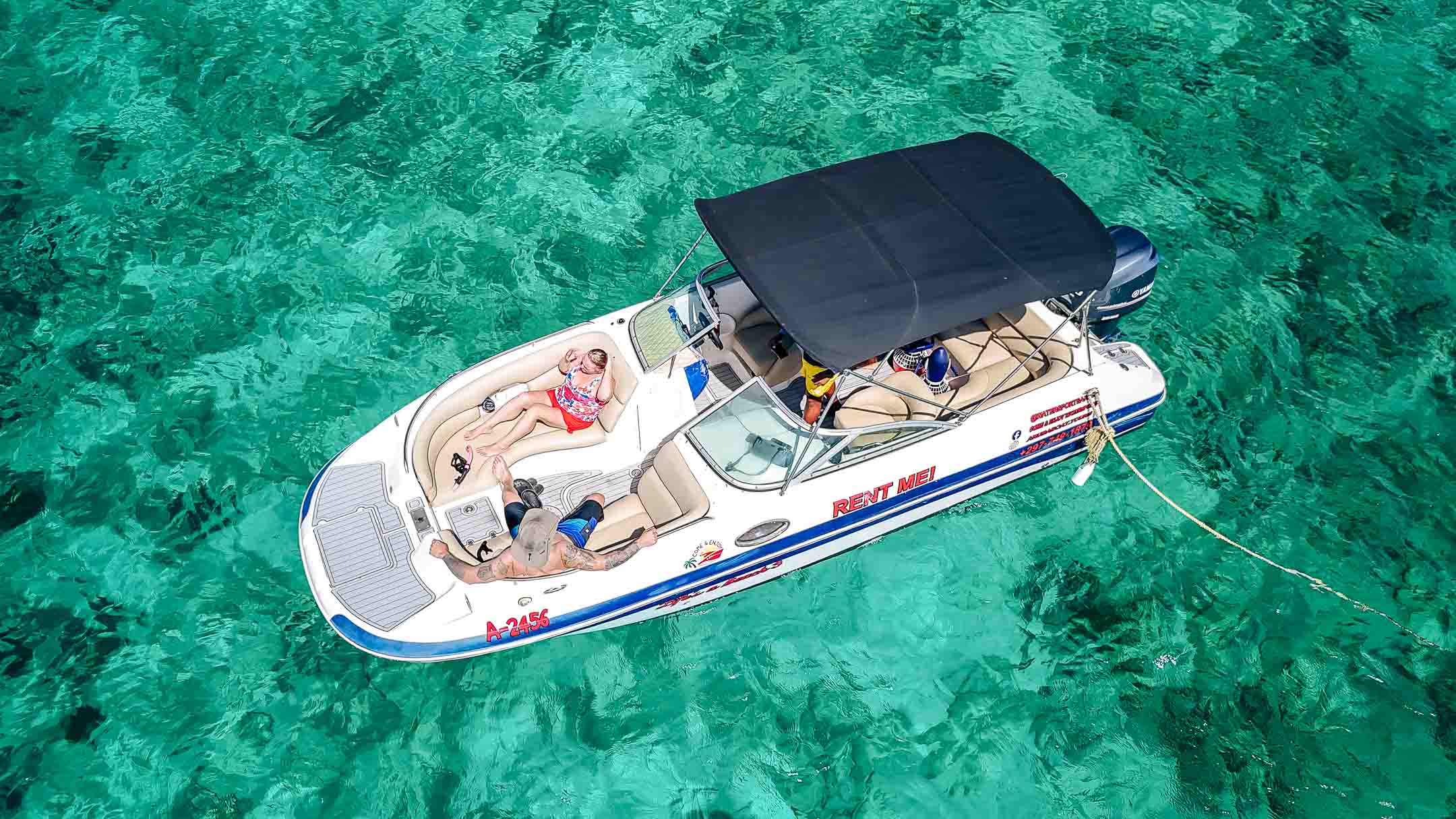 Guests relaxing on the bow of a shaded private charter boat over turquoise water in Aruba